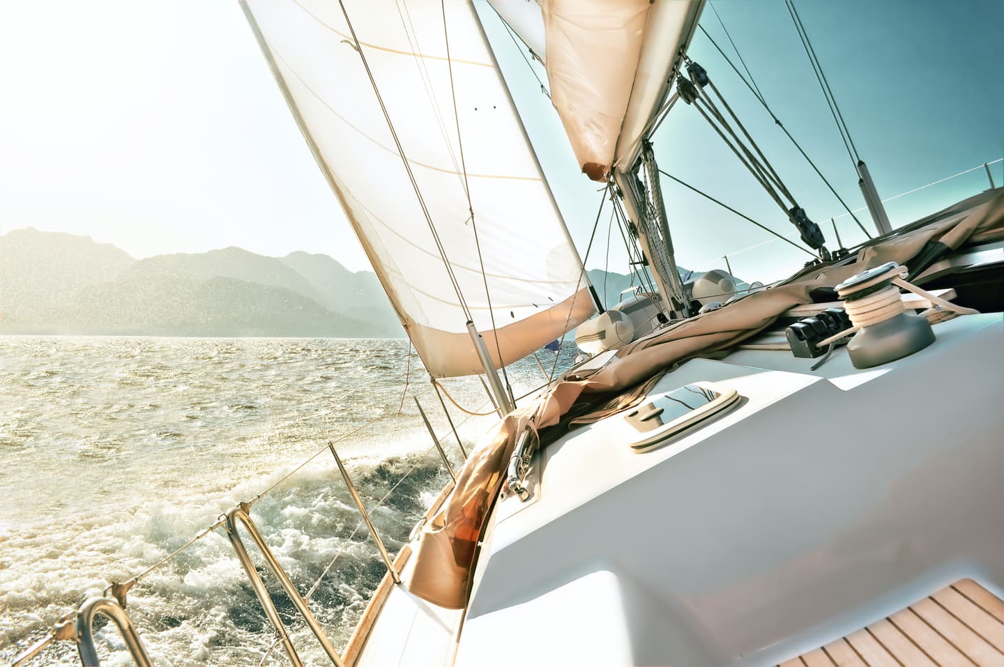 View forward along the deck of a yacht sailing on open water on a sunny day, sails set